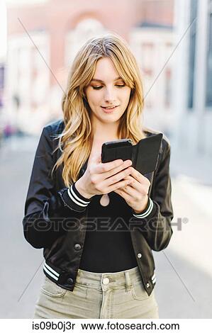 Stock Photography - Young woman in street, using smartphone. Fotosearch