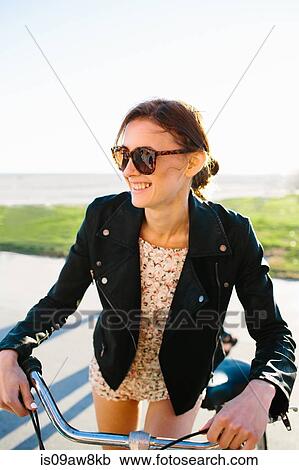 Stock Image - Young woman leaning on bicycle handlebars at coast, Venice Beach, California, USA. Fotosearch