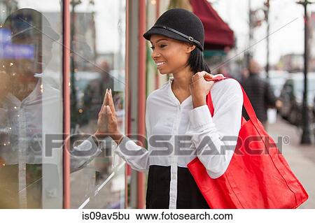 Stock Photograph - Young woman looking in shop window, smiling. Fotosearch