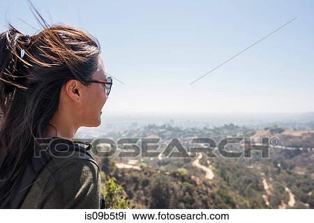 Stock Image - Young woman looking out at landscape from Hollywood sign, Los Angeles, California, USA. Fotosearch