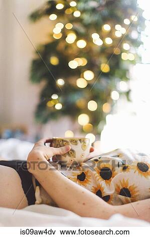 Young woman lying on bed, holding tea cup on stomach, mid section View Large Photo Image Stock Photo - Young woman lying on bed, holding tea cup on stomach, mid section. Fotosearch