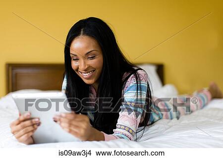 Young woman lying on bed reading digital tablet View Large Photo Image Picture - Young woman lying on bed reading digital tablet. Fotosearch