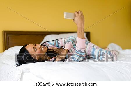 Stock Photography - Young woman lying on bed reading smartphone texts. Fotosearch