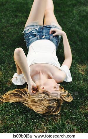 Young woman lying on grass, touching hair View Large Photo Image Stock Image - Young woman lying on grass, touching hair. Fotosearch