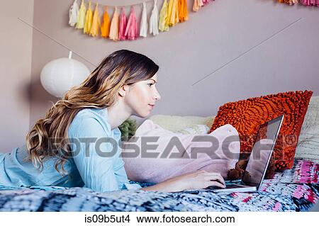 Young woman lying on shabby chic bed looking at laptop View Large Photo Image Picture - Young woman lying on shabby chic bed looking at laptop. Fotosearch