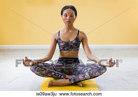 Stock Photograph - Young woman meditating in lotus position on yoga mat. Fotosearch