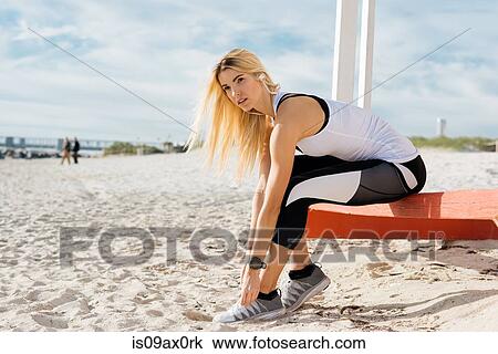Young woman on beach, tying shoelace, wearing earphones View Large Photo Image Stock Image - Young woman on beach, tying shoelace, wearing earphones. Fotosearch
