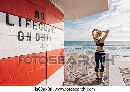 Stock Image - Young woman on lifeguard platform, looking at view, rear view. Fotosearch