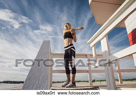 Stock Photograph - Young woman on lifeguard platform, exercising, low angle view. Fotosearch
