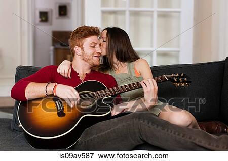 Young woman on sofa kissing young man playing guitar on cheek View Large Photo Image Stock Photo - Young woman on sofa kissing young man playing guitar on cheek. Fotosearch