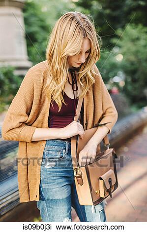 Young woman outdoors, opening satchel style bag View Large Photo Image Stock Image - Young woman outdoors, opening satchel style bag. Fotosearch