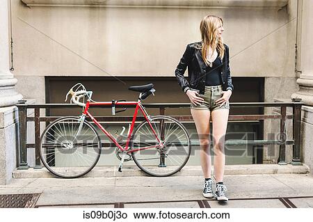 Young woman outdoors, standing on pavement, looking along street View Large Photo Image Picture - Young woman outdoors, standing on pavement, looking along street. Fotosearch