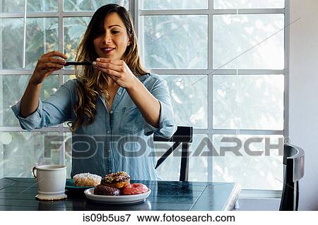 Stock Photo - Young woman photographing doughnut holes on table. Fotosearch