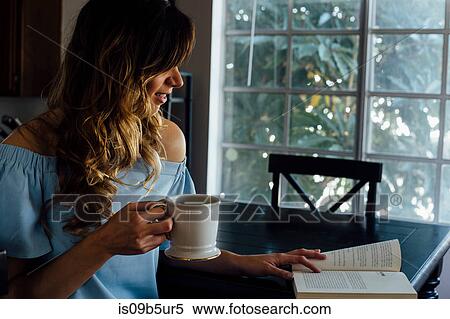 Stock Photography - Young woman reading book at table. Fotosearch