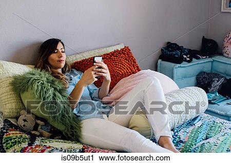 Young woman reclining on shabby chic bed looking at smartphone View Large Photo Image Stock Image - Young woman reclining on shabby chic bed looking at smartphone. Fotosearch