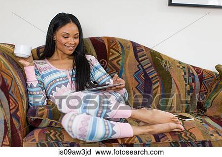 Young woman reclining on sofa drinking coffee and reading digital tablet View Large Photo Image Stock Image - Young woman reclining on sofa drinking coffee and reading digital tablet. Fotosearch