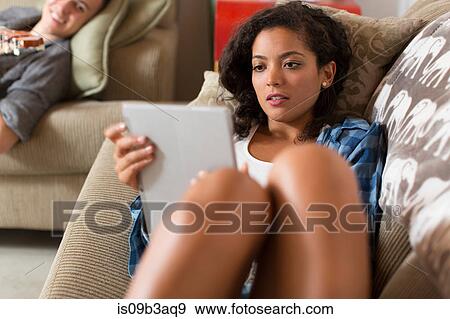 Young woman relaxing on sofa using digital tablet View Large Photo Image Stock Photo - Young woman relaxing on sofa using digital tablet. Fotosearch