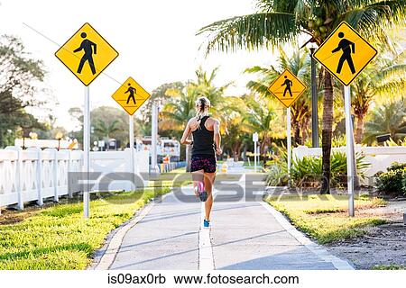 Stock Image - Young woman running along pathway, rear view. Fotosearch