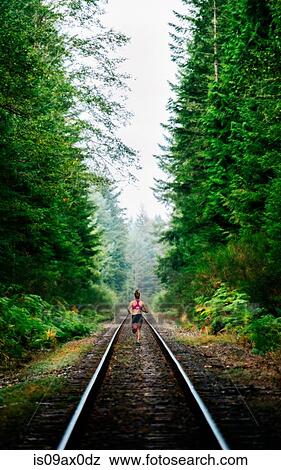 Stock Photo - Young woman running along rural train track, rear view. Fotosearch