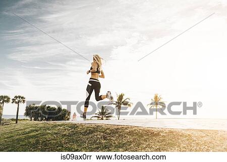 Stock Photography - Young woman running outdoors, rear view, low angle view. Fotosearch