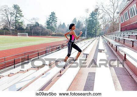 Picture - Young woman running up steps at sports track. Fotosearch