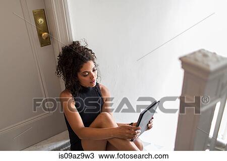Young woman sitting at top of stairs, using digital tablet View Large Photo Image Stock Image - Young woman sitting at top of stairs, using digital tablet. Fotosearch
