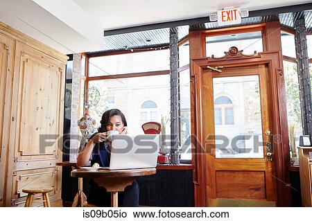 Picture - Young woman sitting in cafe, drinking coffee, using laptop. Fotosearch
