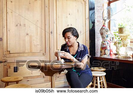 Stock Image - Young woman sitting in cafe, drinking coffee. Fotosearch
