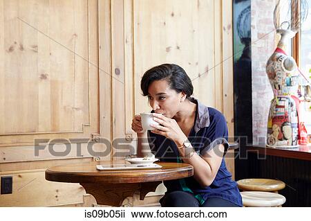 Stock Image - Young woman sitting in cafe, drinking coffee. Fotosearch