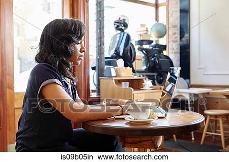 Picture - Young woman sitting in cafe, using laptop. Fotosearch