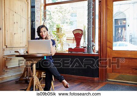 Young woman sitting in cafe, using laptop and smartphone View Large Photo Image Stock Image - Young woman sitting in cafe, using laptop and smartphone. Fotosearch