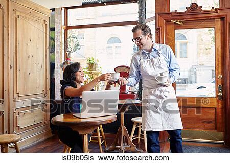 Young woman sitting in cafe, using laptop, male worker taking empty coffee cup View Large Photo Image Stock Photograph - Young woman sitting in cafe, using laptop, male worker taking empty coffee cup. Fotosearch