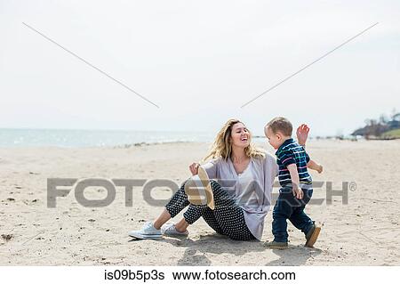 Young woman sitting on beach playing with toddler son View Large Photo Image Stock Photograph - Young woman sitting on beach playing with toddler son. Fotosearch