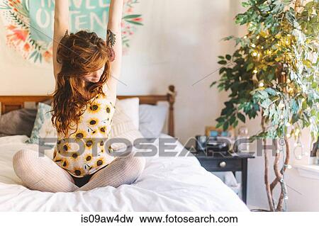 Young woman sitting on bed, arms outstretched View Large Photo Image Stock Photo - Young woman sitting on bed, arms outstretched. Fotosearch