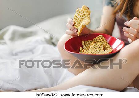Young woman, sitting on bed, eating snack food from bowl, mid section View Large Photo Image Stock Image - Young woman, sitting on bed, eating snack food from bowl, mid section. Fotosearch