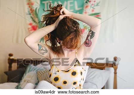Young woman sitting on bed, putting hair up in ponytail View Large Photo Image Stock Photography - Young woman sitting on bed, putting hair up in ponytail. Fotosearch