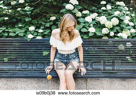 Young woman sitting on bench, holding yellow rose, looking away View Large Photo Image Stock Photo - Young woman sitting on bench, holding yellow rose, looking away. Fotosearch