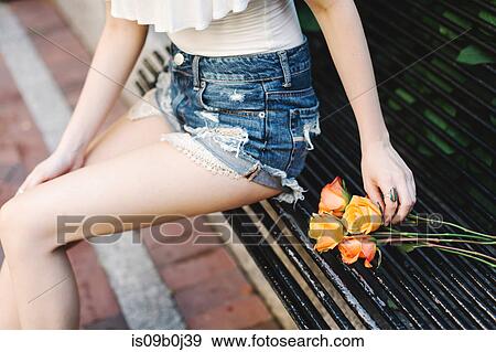Young woman sitting on bench, roses beside her, mid section View Large Photo Image Stock Photo - Young woman sitting on bench, roses beside her, mid section. Fotosearch