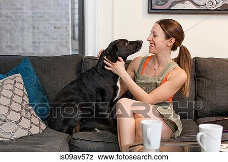 Young woman sitting on sofa face to face with pet dog smiling View Large Photo Image Stock Photo - Young woman sitting on sofa face to face with pet dog smiling. Fotosearch