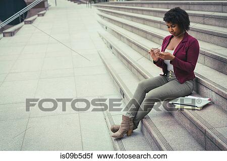 Young woman sitting on steps, using smartphone View Large Photo Image Stock Image - Young woman sitting on steps, using smartphone. Fotosearch