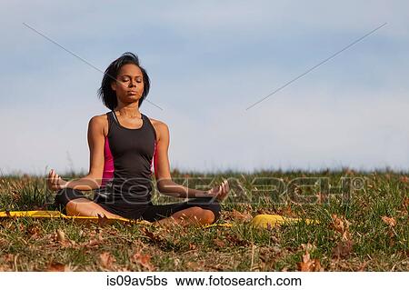 Young woman sitting on yoga mat, outdoors, in lotus position View Large Photo Image Stock Photograph - Young woman sitting on yoga mat, outdoors, in lotus position. Fotosearch