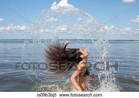 Stock Photography - Young woman splashing and throwing back long hair from sea, Santa Rosa Beach, Florida, USA. Fotosearch