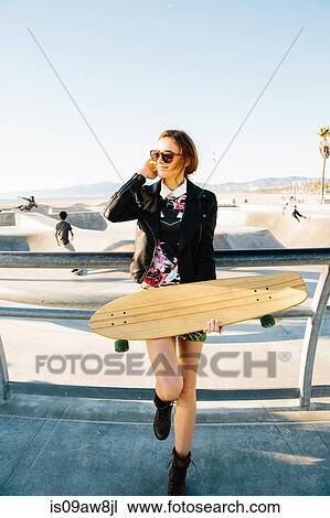 Young woman standing by railings, near skate park, holding skateboard View Large Photo Image Stock Image - Young woman standing by railings, near skate park, holding skateboard. Fotosearch