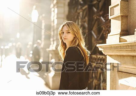 Young woman standing in street, looking over shoulder, pensive expression View Large Photo Image Stock Photography - Young woman standing in street, looking over shoulder, pensive expression. Fotosearch