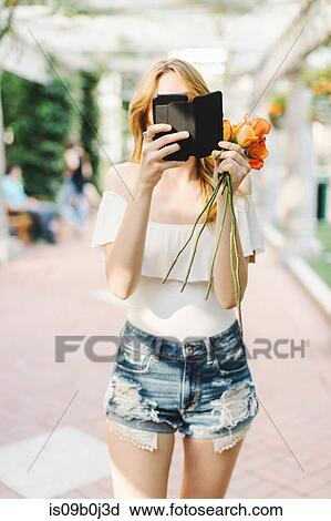Young woman standing outdoors, holding roses, using smartphone View Large Photo Image Stock Image - Young woman standing outdoors, holding roses, using smartphone. Fotosearch