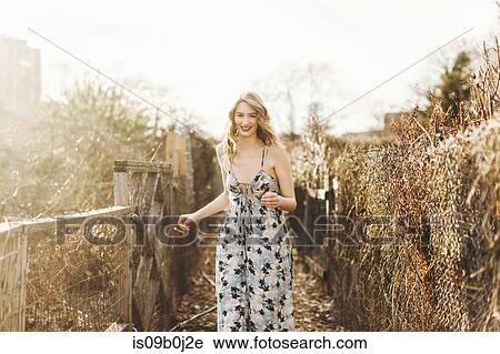 Stock Image - Young woman walking along rural farm pathway, smiling. Fotosearch