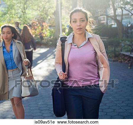 Stock Image - Young woman walking through city park. Fotosearch