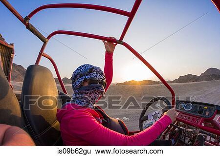 Stock Photograph - Young woman with head wrapped in scarf driving beach buggy in desert, Hurghada, Al Bahr al Ahmar, Egypt. Fotosearch