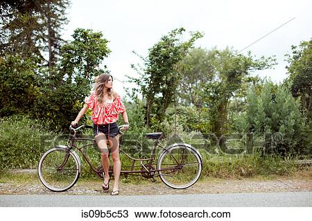 Young woman with tandem bicycle looking over her shoulder on rural road View Large Photo Image Stock Image - Young woman with tandem bicycle looking over her shoulder on rural road. Fotosearch