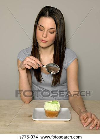 Picture - Young woman looking at cake with magnifying glass. Fotosearch